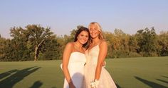 two beautiful women standing next to each other on top of a green field with trees in the background