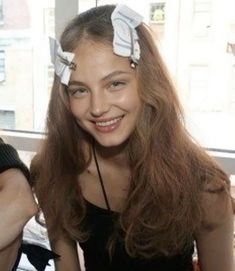 a woman with long hair and two bows on her head smiles at the camera while sitting in front of a window