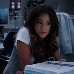 a woman sitting at a desk with stacks of papers in front of her, looking down