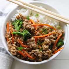 a white bowl filled with meat and veggies next to chopsticks on top of rice