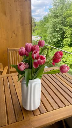 a white vase filled with pink tulips sitting on top of a wooden table