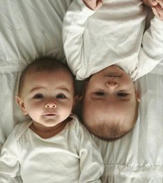 two babies laying next to each other on top of a white bed covered in sheets