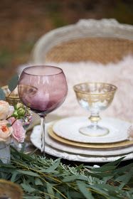 two wine glasses sitting on top of a table next to plates and flowers in vases