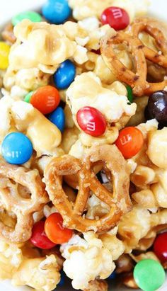 a bowl filled with candy corn and m & ms pretzels on the side