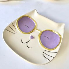 a white cat with purple glasses on it's face is sitting on a plate