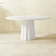 a white round table on a tiled floor in front of a wall with a potted plant