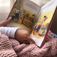 a child is reading a book while sitting on a bed with pink blanket and white leggings