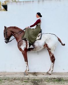 a woman riding on the back of a brown and white horse next to a wall