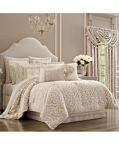 a bed covered in white and beige comforter next to a vase with flowers on it