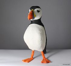 a stuffed bird with an orange beak and black head is standing on a white surface