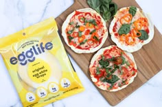 three small pizzas sitting on top of a cutting board next to a bag of egglite