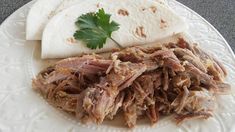 a white plate topped with meat and tortilla bread next to a garnish