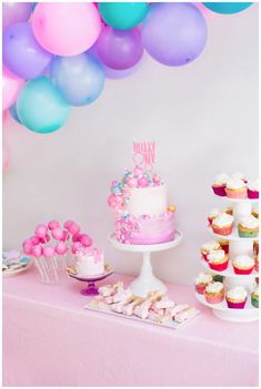 a table topped with lots of cupcakes and cake next to balloons in the air