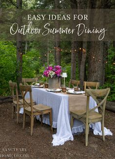 an outdoor dinner table set up in the woods with pink flowers and candles on it