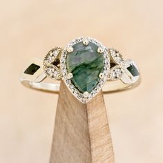 a pear shaped green and white diamond ring on top of a piece of wood with diamonds around it