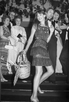 a black and white photo of a woman in a dress holding a basket while standing on steps