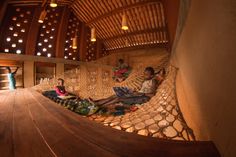 two people sitting on a hammock in a room with wooden floors and walls