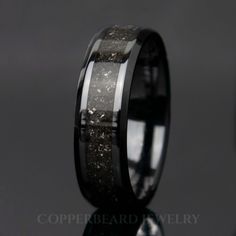 a wedding ring with black ceramic and silver inlays, on a reflective surface