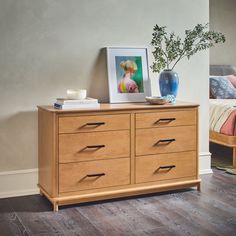 a wooden dresser with two vases on top of it next to a small bed