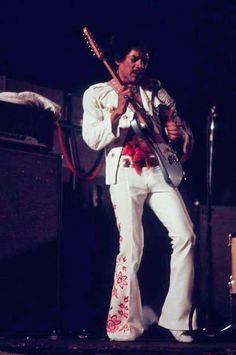 a man with an electric guitar in his hand and wearing white pants, standing on stage