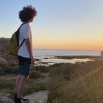 a woman standing on top of a rock next to the ocean with a yellow backpack