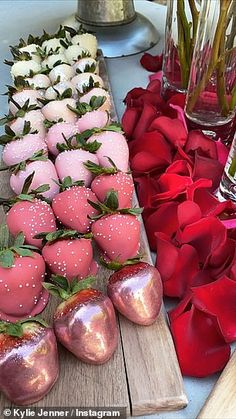 there are many strawberries on the wooden board next to each other and flowers in vases