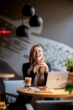 a woman sitting at a table with a laptop in front of her smiling and looking up