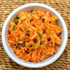 a white bowl filled with carrots and raisins on top of a wicker table