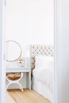 a bedroom with a white bed, nightstand and round mirror on the wall above it