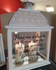 two lit candles in a white lantern with french writing on the front and back sides