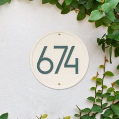 a white house number sign sitting on the side of a wall covered in green leaves