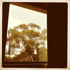 the view from inside an open window looking at trees and skyscrapers in the distance