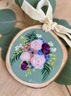 a painted plate with flowers and leaves on it next to a white ribbon tied around the edge