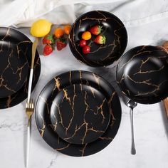 four black marbled plates with forks and knives on a white table cloth next to fruit