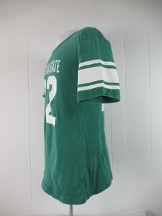 "Vintage 1970s or 80s college t shirt. Made of green cotton with thick white college graphics: Michigan State #22. Has Champion blue block label. Size large. Actual measurements are: 39\" around the chest 39\" around the waist 20\" shoulder seam to shoulder seam 28\" overall length In very good condition with 3\" of seam repair to the cuff." Retro Crew Neck T-shirt For School, Green Short Sleeve T-shirt For College, Collegiate Green T-shirt With Logo Print, Retro Green T-shirt For Fans, Retro Green T-shirt For Streetwear, Retro College T-shirt With Screen Print, Varsity Cotton Tops For School, Cotton Varsity Tops For School, Green Collegiate T-shirt With Letter Print