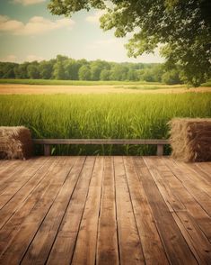 an empty wooden deck with hay bales in the foreground and a green field behind it