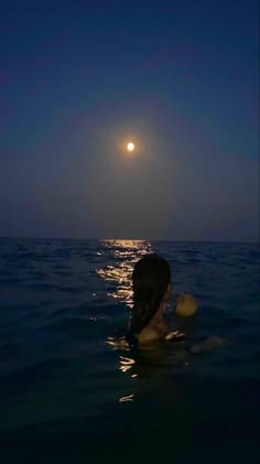 a woman swimming in the ocean at night with the moon shining over her head and back