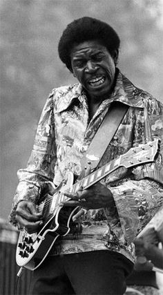 a black and white photo of a man playing an electric guitar with his mouth open