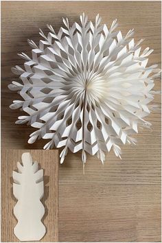 a white paper flower sitting on top of a wooden table next to a cut out piece of paper