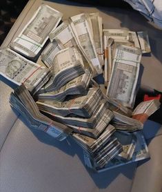 a pile of money sitting on top of a seat in front of a person holding a cell phone