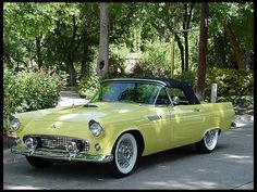 an old yellow car parked on the side of the road in front of some trees