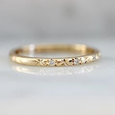 a yellow gold wedding band with three diamonds on the top and bottom, sitting on a white surface