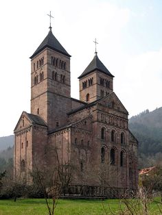 an old church in the middle of a green field with mountains in the back ground