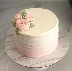 there is a white cake with pink flowers on the top and bottom layer, sitting on a wooden plate