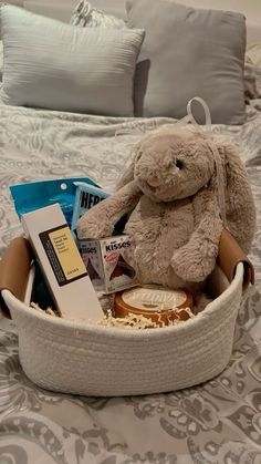 a stuffed animal sitting in a basket on top of a bed with books and snacks