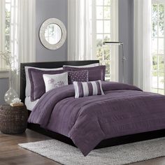 a bed with purple comforter and pillows in a room