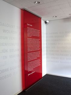 a red glass door in the corner of a room with white walls and black carpet