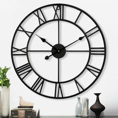 a large black clock sitting on top of a table next to vases and books