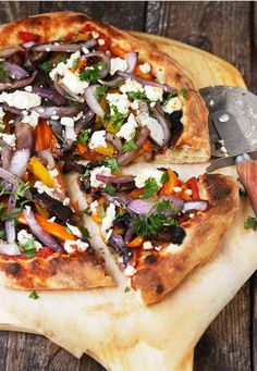 a pizza sitting on top of a wooden cutting board next to a knife and fork