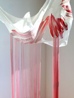 a pink and white sculpture is hanging from the ceiling in front of a wall with curtains on it